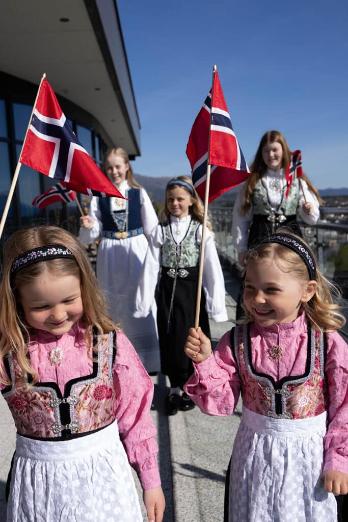 Barn som går i festdrakt og flagg ute på terrassen i 9. etasje på Stord Hotell.